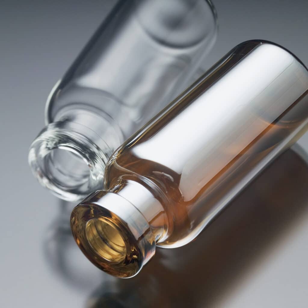 A clear glass vial and Siltek treated vial lying beside each other.