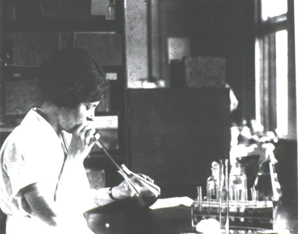 a black and white photo of a woman in a laboratory mouth pipetting